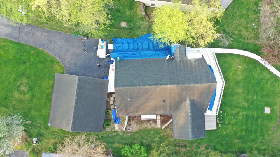 Aerial view of a home before replacing the roof, roofers are applying a blue tarp to the roof