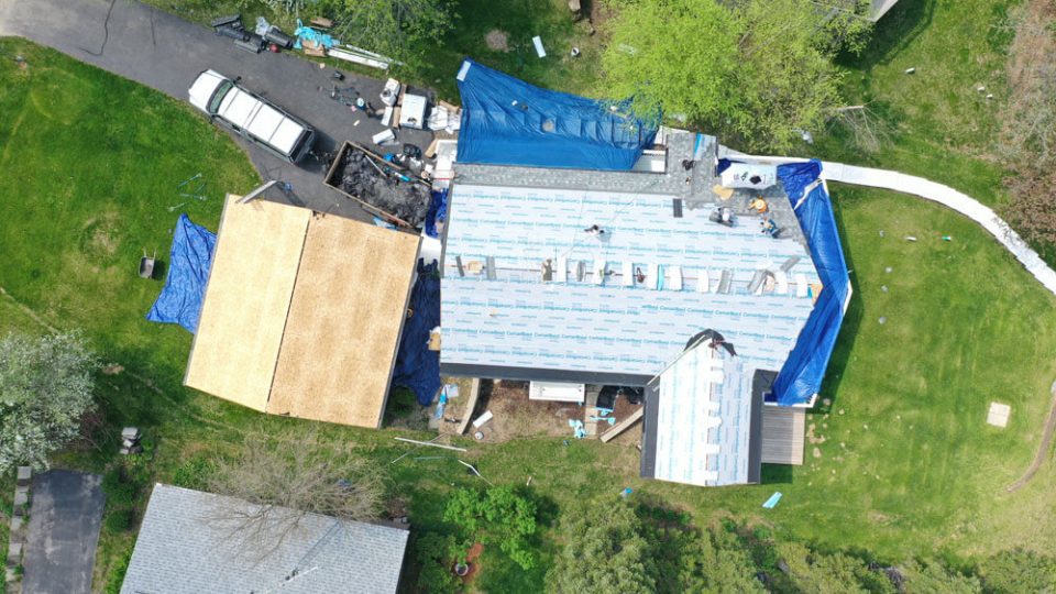 Aerial view of a home while roofers are starting to install gray asphalt shingles