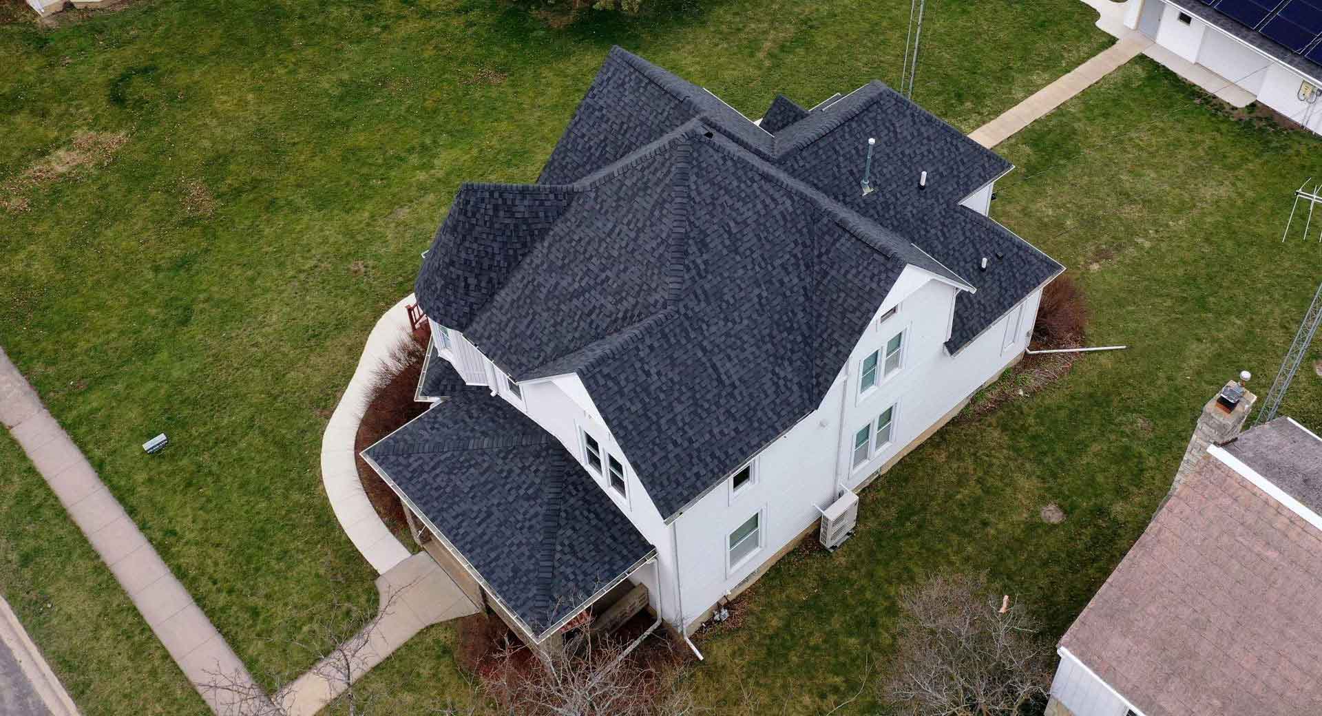 Aerial view of a home - white siding and a dark charcoal asphalt roof after a roof replacement