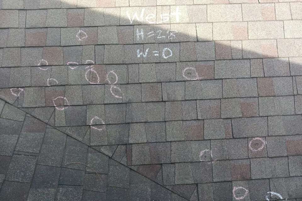 Close up of a rooftop with chalk circles drawn around damaged shingles
