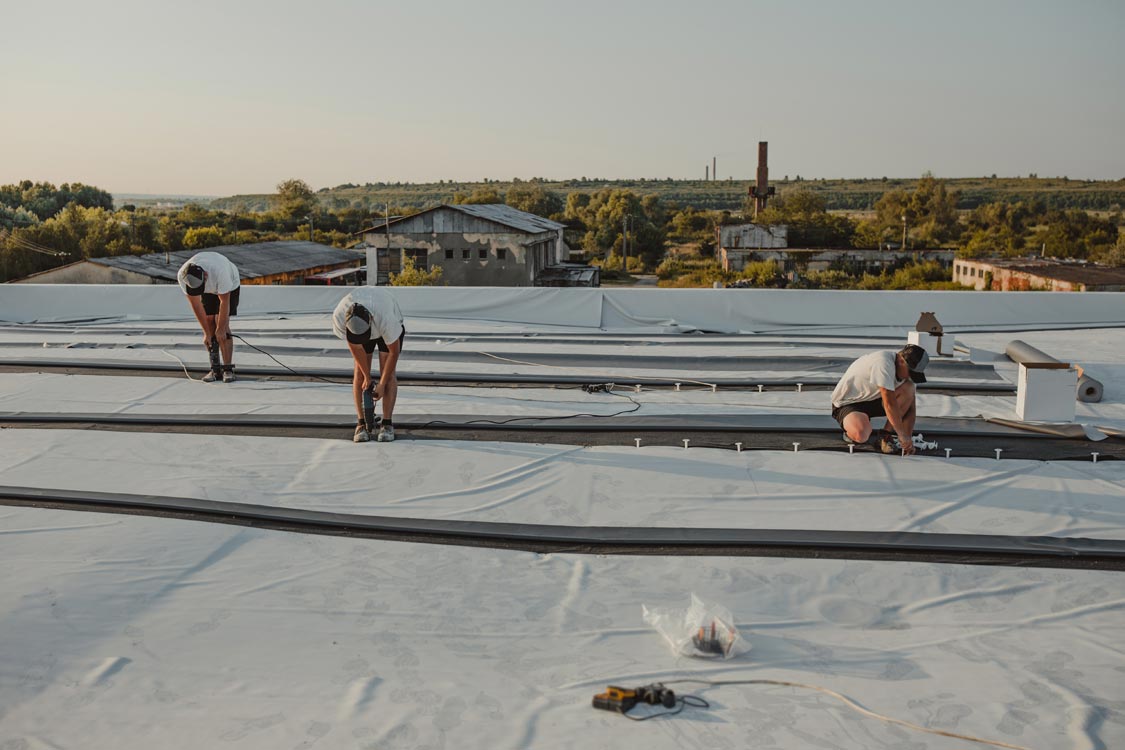 3 roofers installing the underlayment on a commercial roof